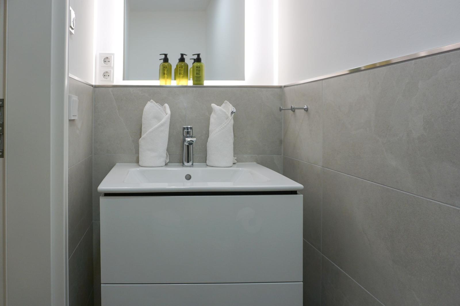 Waschbecken mit Spiegel, Handtüchern und Seifenspender.