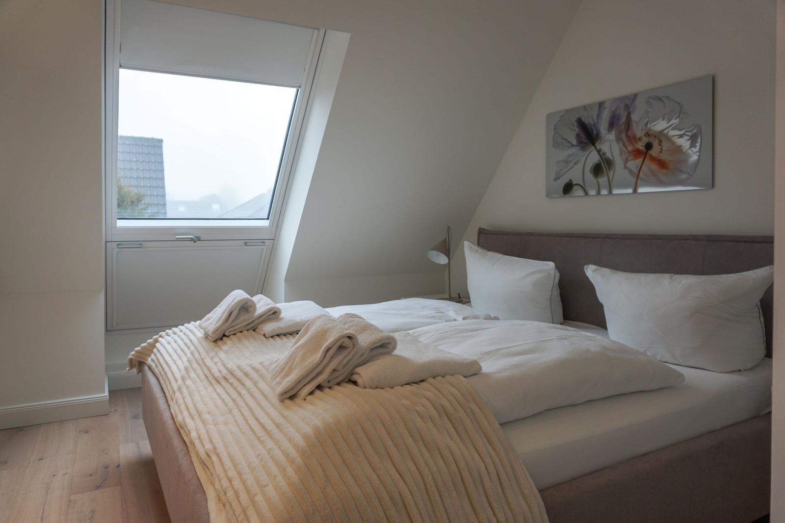 Schlafzimmer mit Dachschrägen, Bett, Fenster und Wandbild.