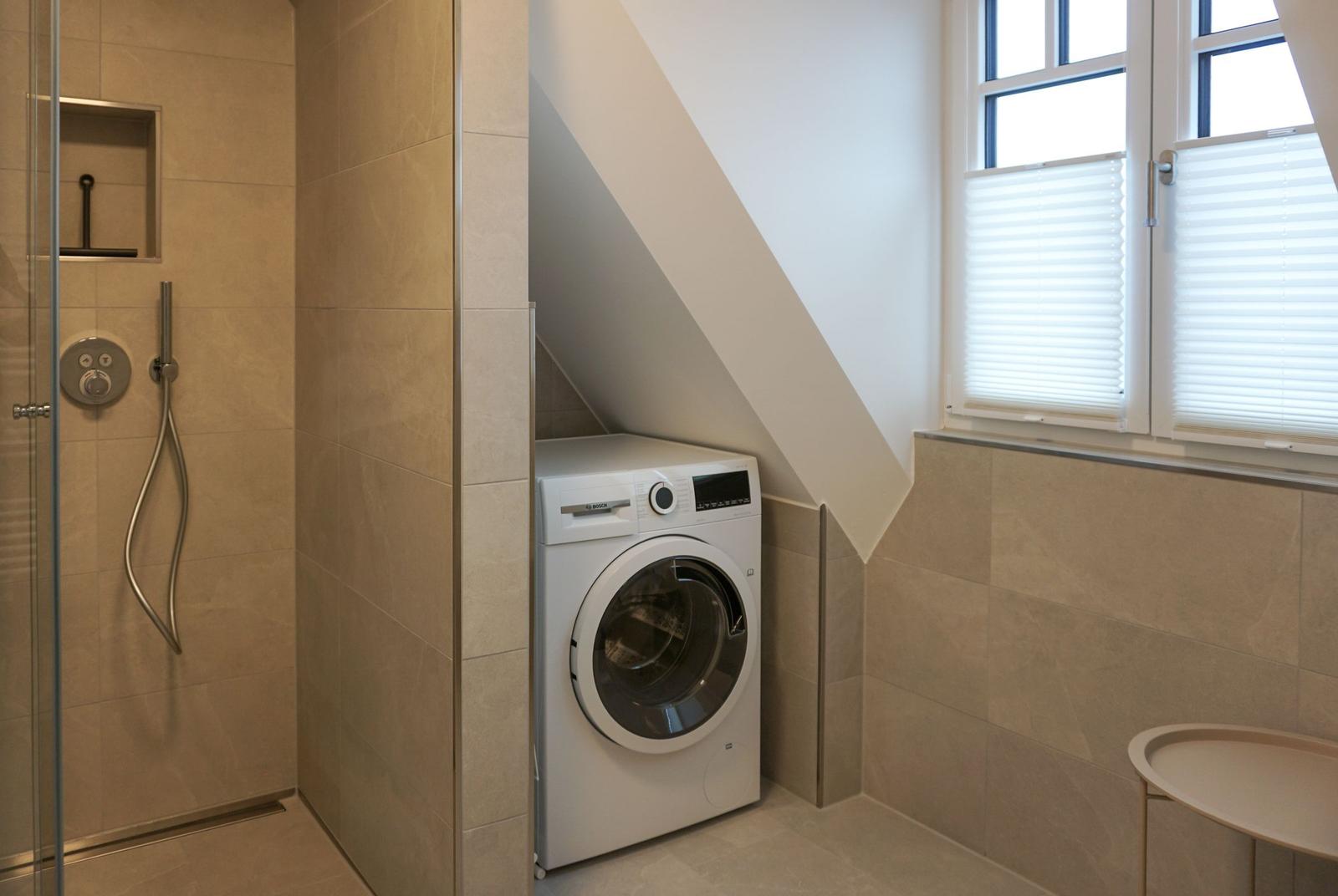 Waschmaschine unter Dachschrägen, Dusche mit Glaswand und Fenster mit Jalousie.