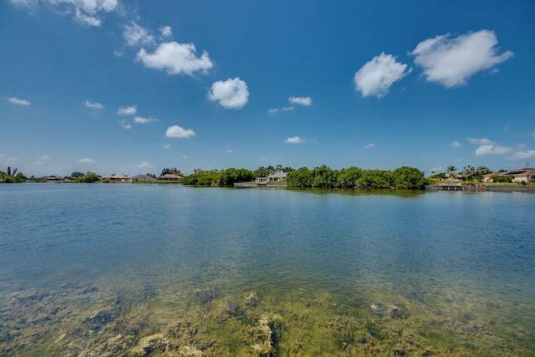 Klarer See mit grüner Vegetation und Häusern am Ufer unter blauem Himmel mit weißen Wolken.