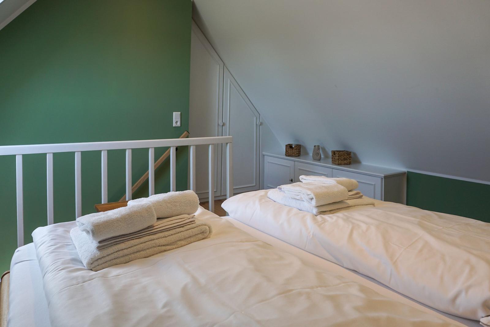 Two beds with white bedding and folded towels in an attic room with green wall.