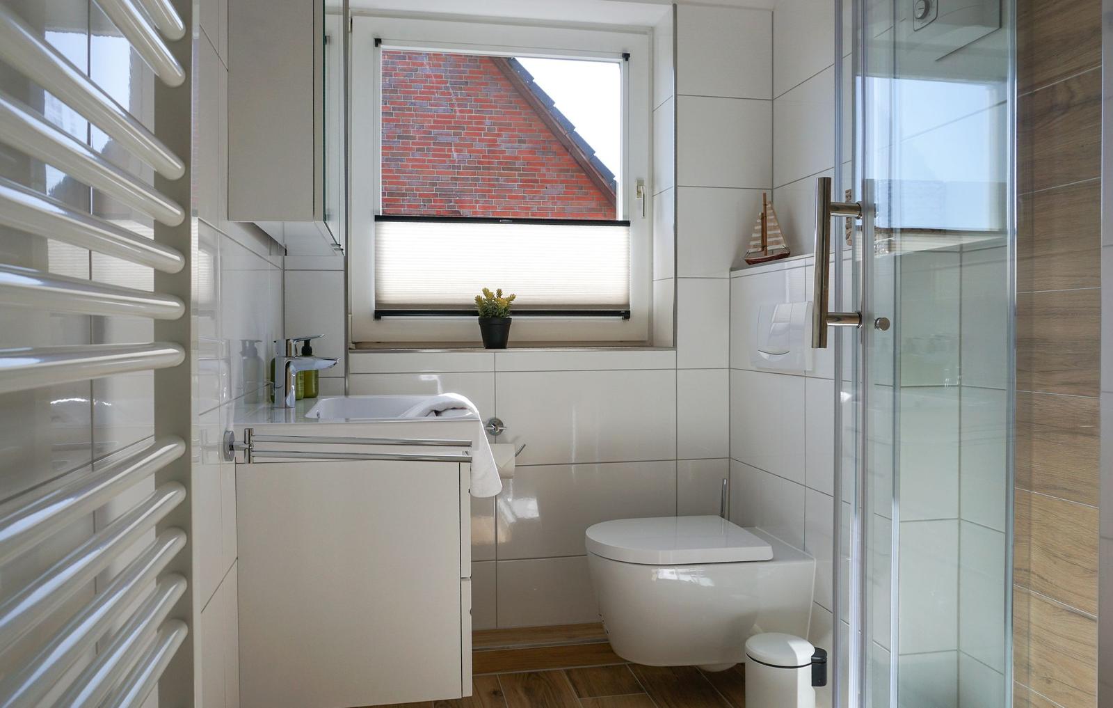 Bathroom with shower, toilet, and sink. Window with view of brick wall.