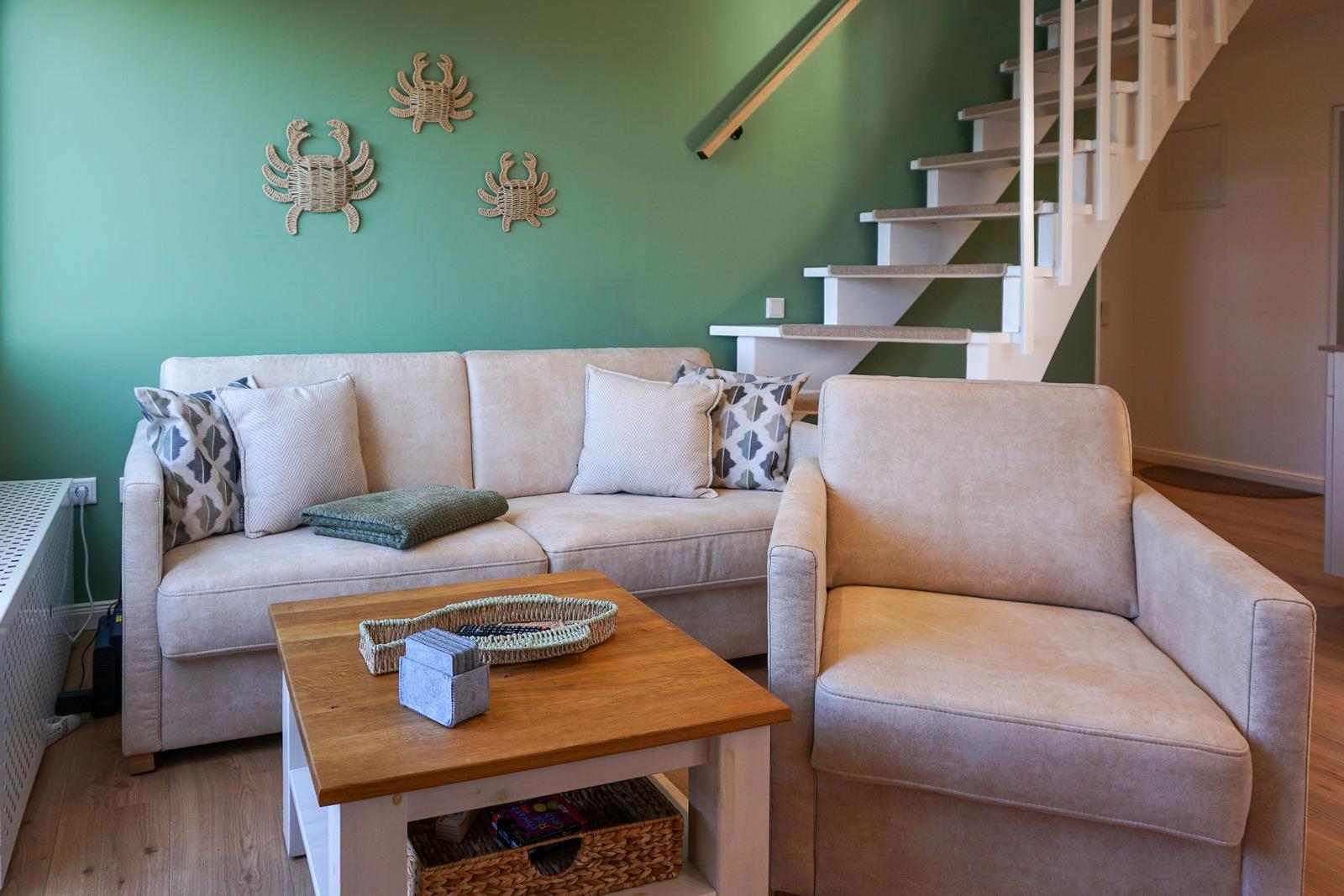 Living room with sofa, armchair, and wooden table. Green wall with crab decor. Staircase in background.
