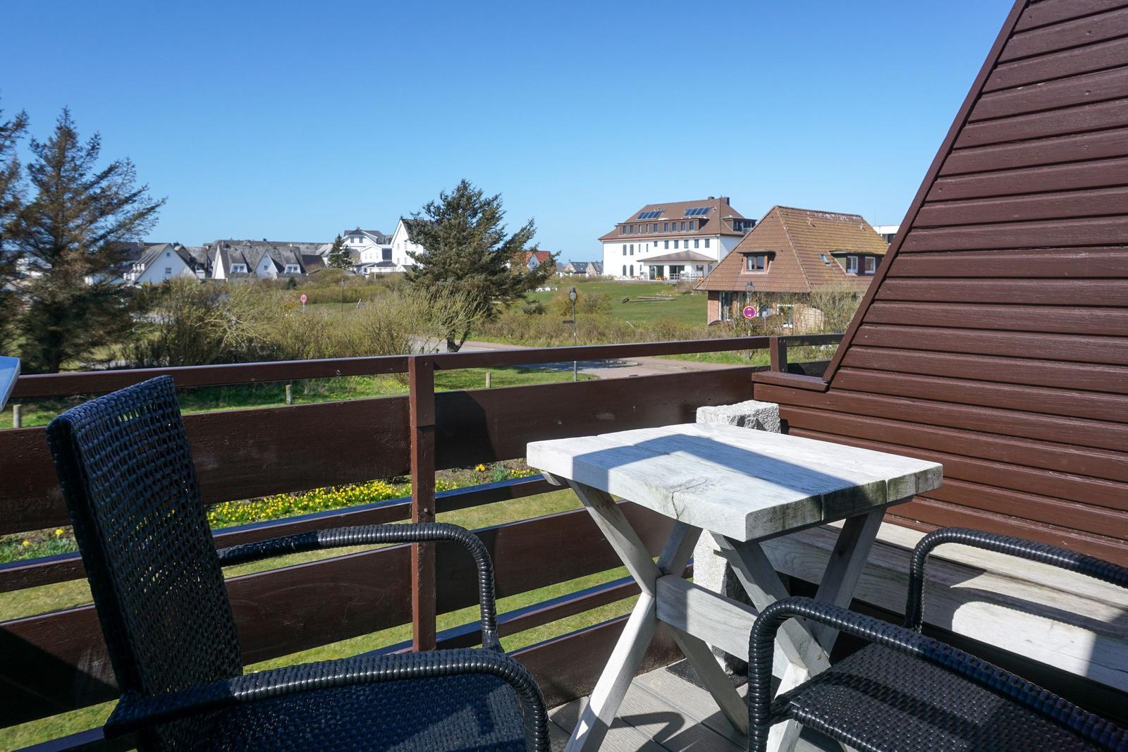 Terrace with table and chairs, view of green areas and houses.