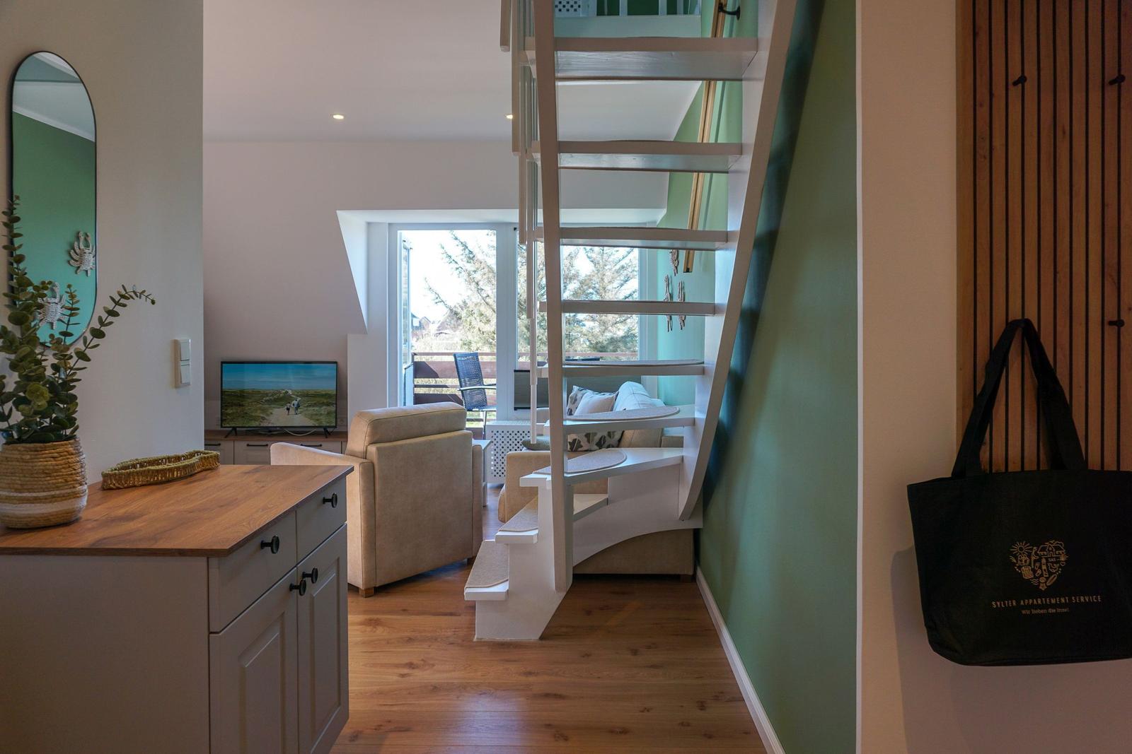 Entrance area with wooden staircase and living area with TV and window.
