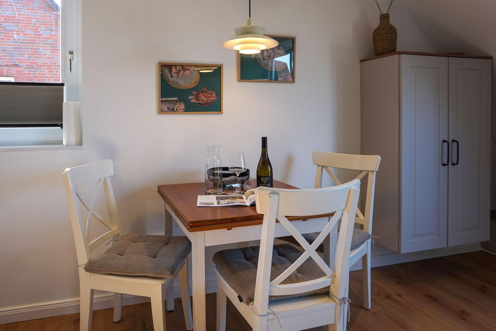 Dining table with three chairs, wall art, and cabinet in room.