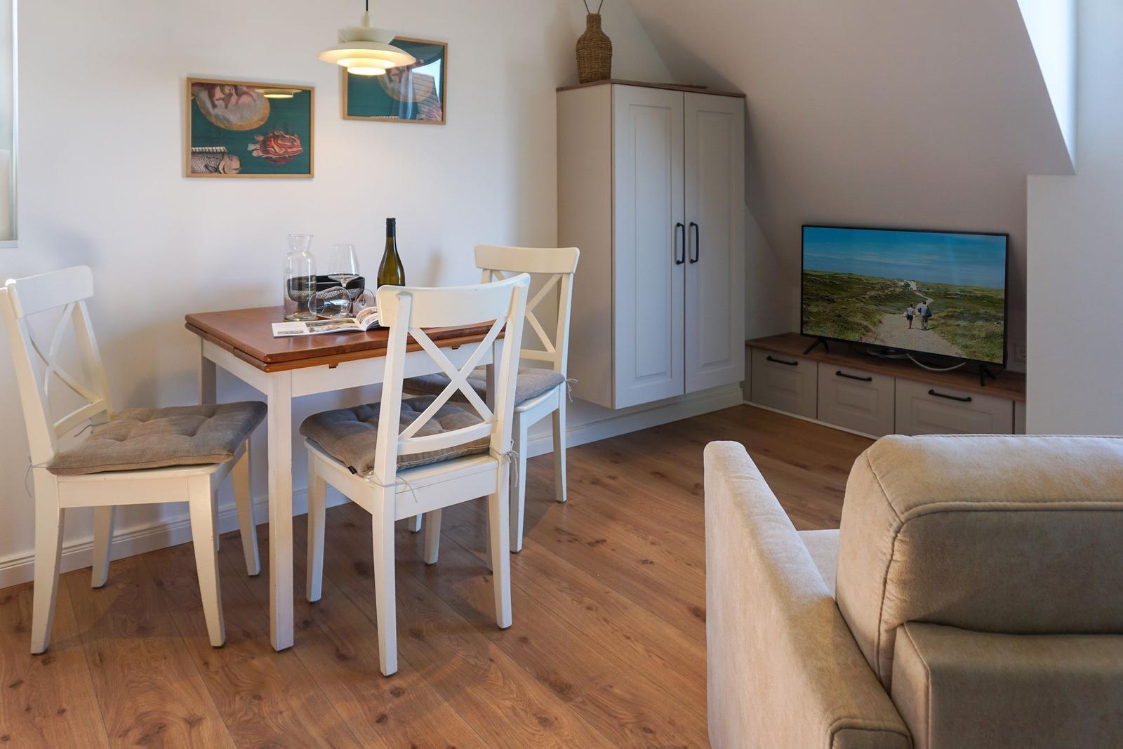 Dining area with table, chairs, and TV in a room with hardwood floor and cabinet.