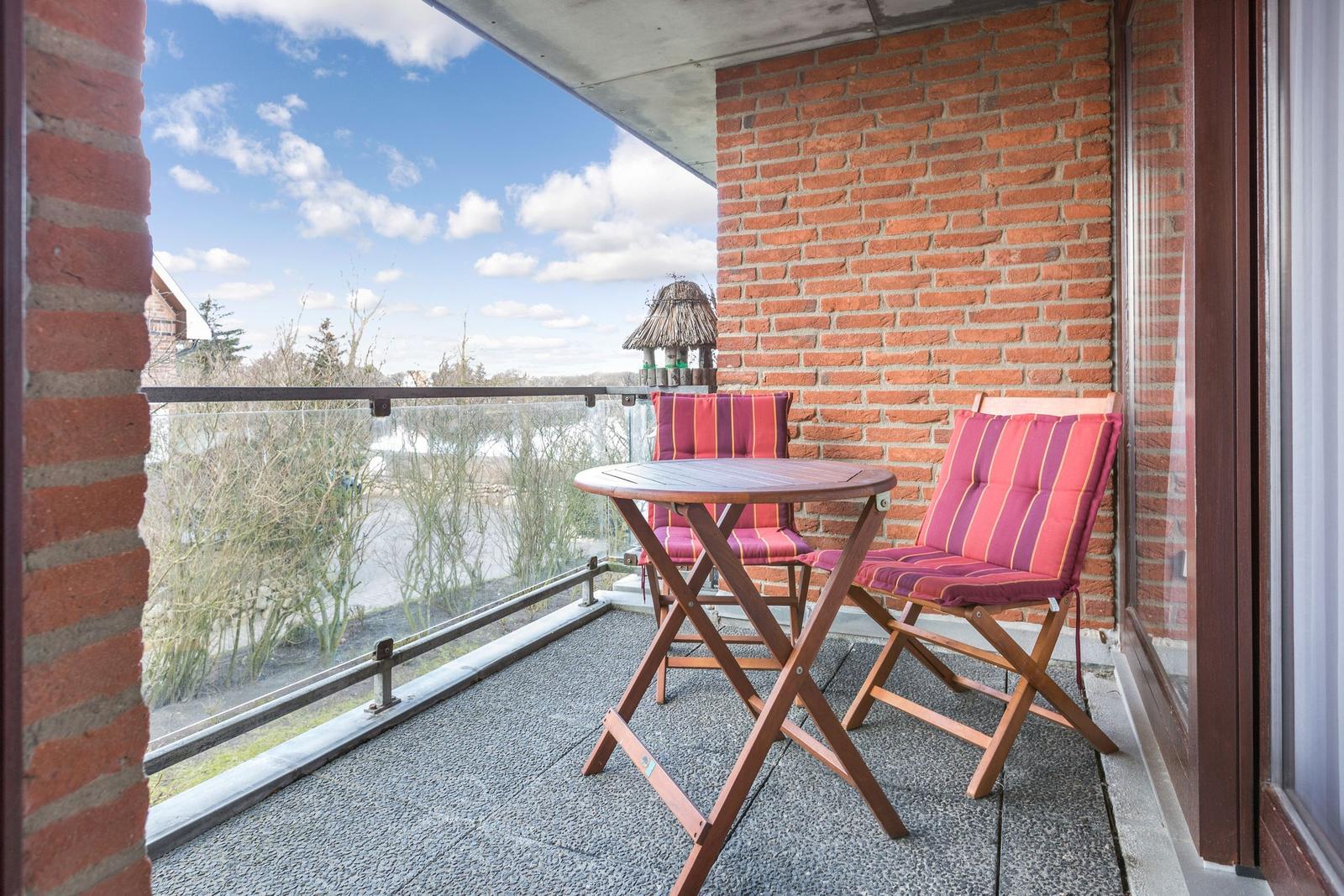 Terrace with table and two chairs with colorful cushions. View of water and trees.