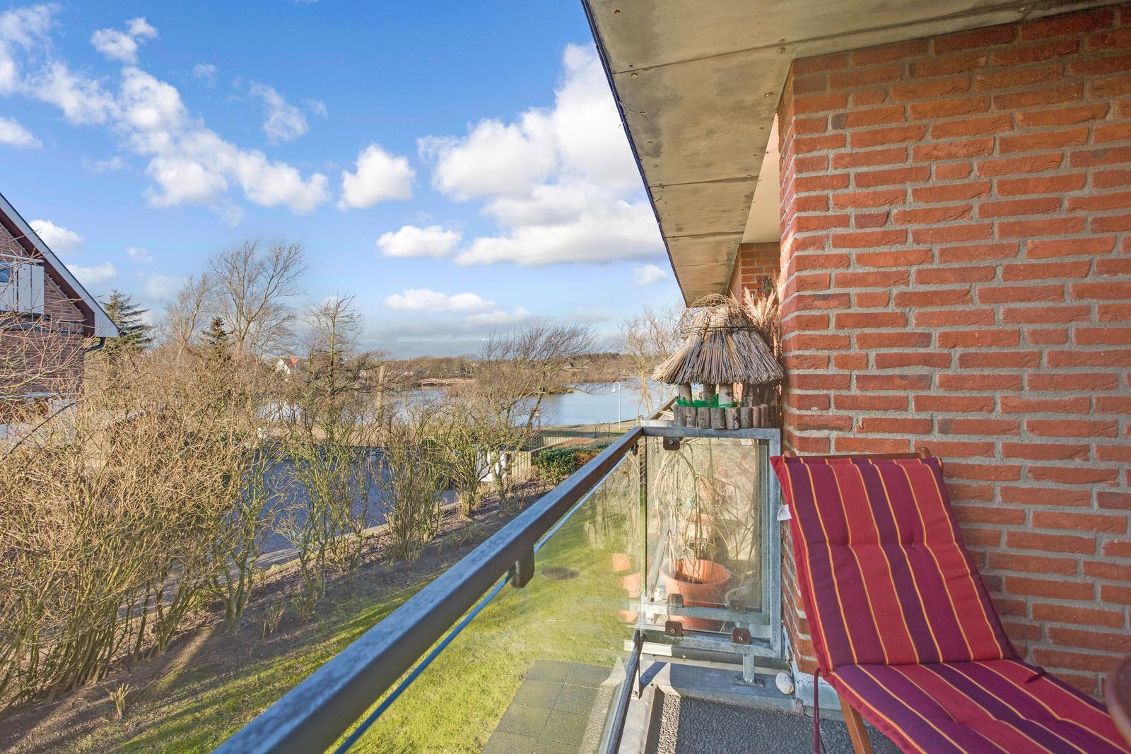 Balcony with lounge chair and view of water and trees.