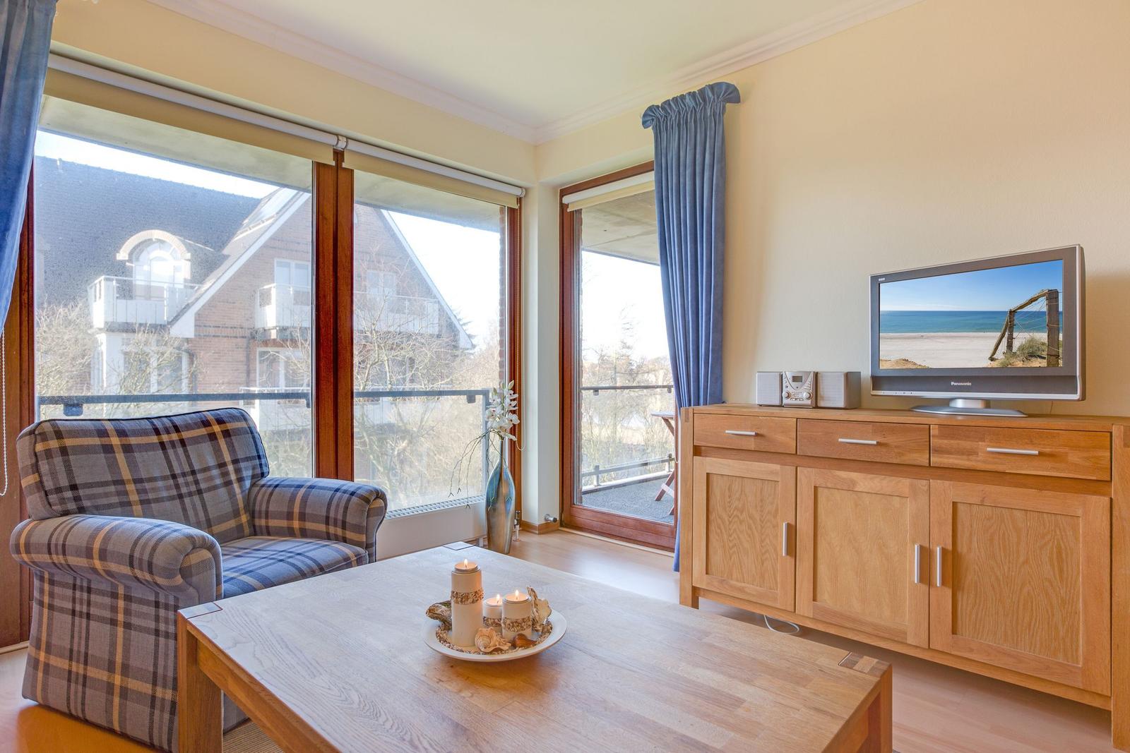 Living room with armchair, coffee table, and TV. Large windows with balcony view.