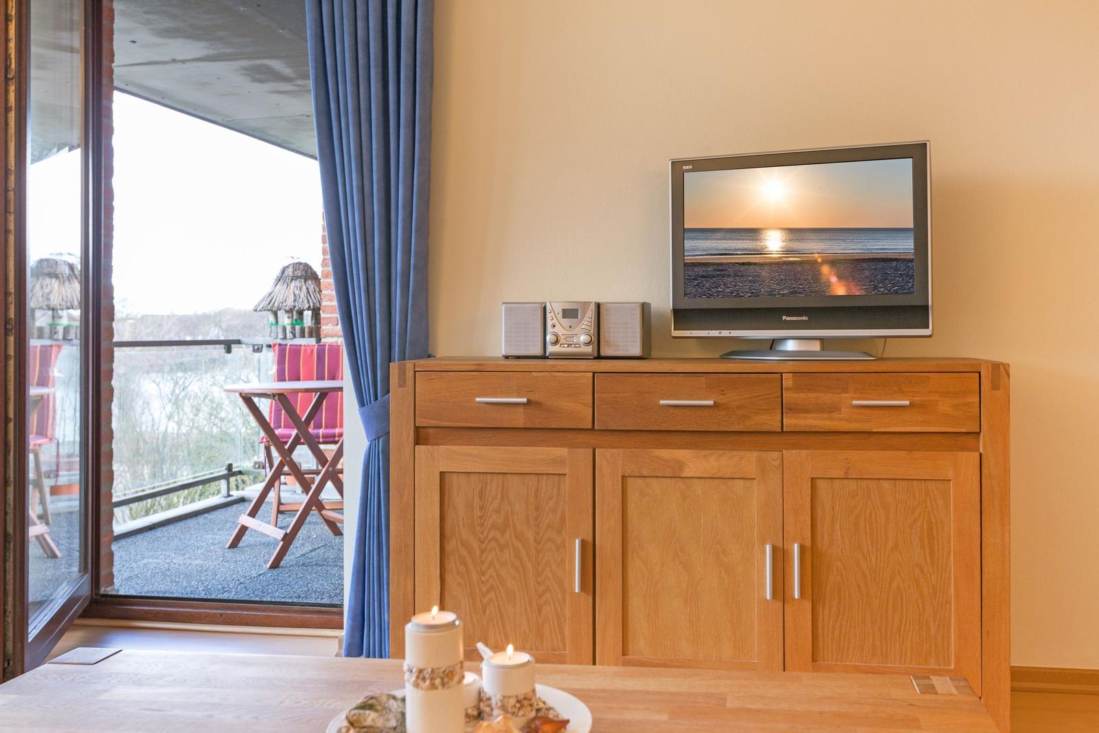 TV on wooden cabinet, balcony with chairs and table