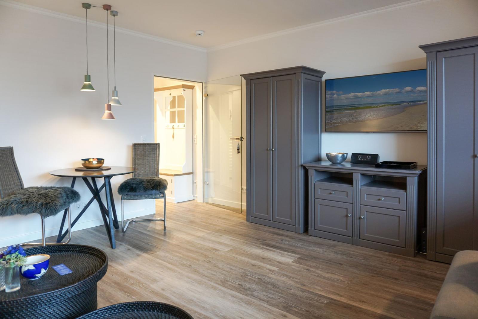 Wohnraum mit grauem Schrank, Tisch, Stühlen und Wandbild.