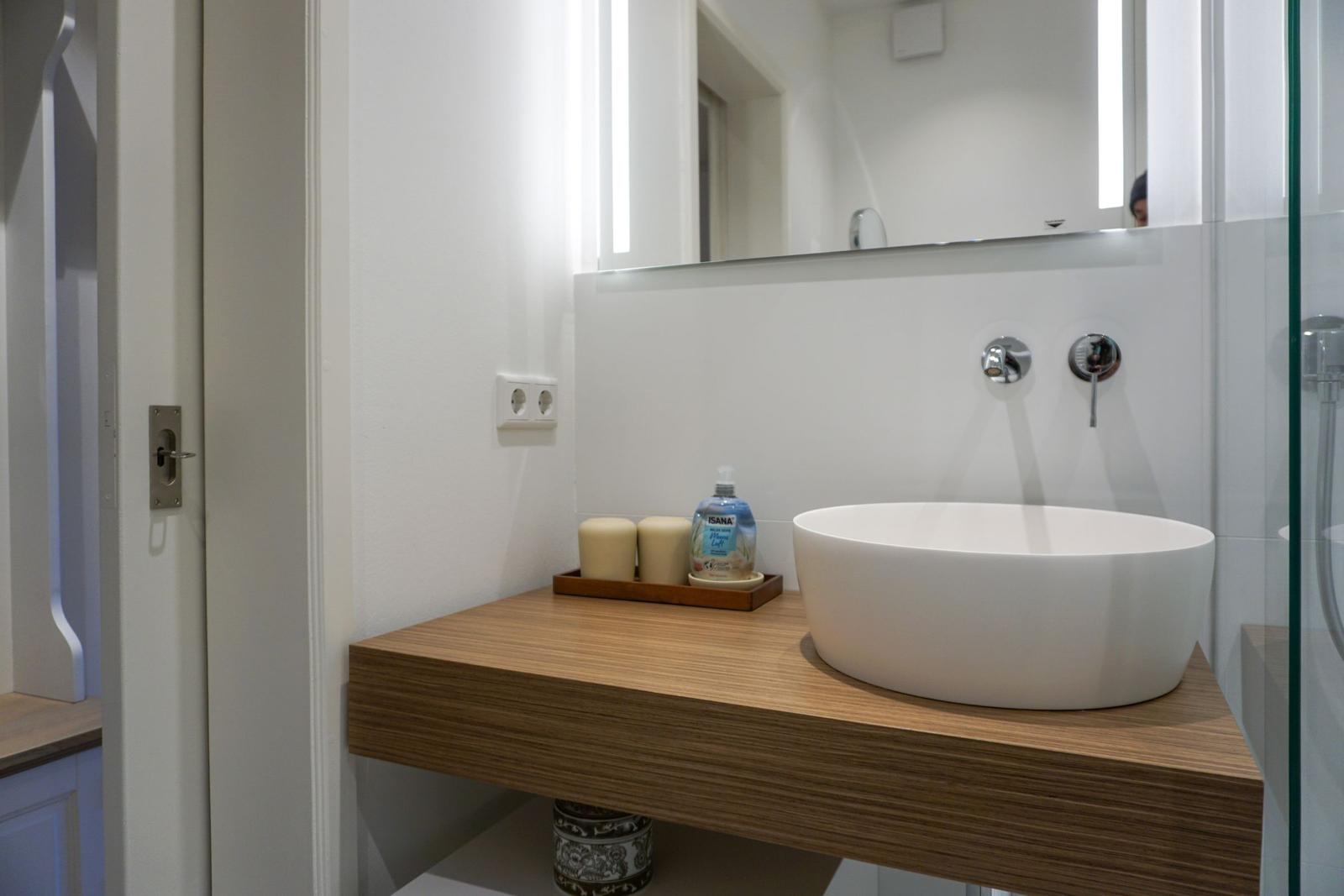 Waschbecken auf Holzunterschrank mit Spiegel und Duschbereich.