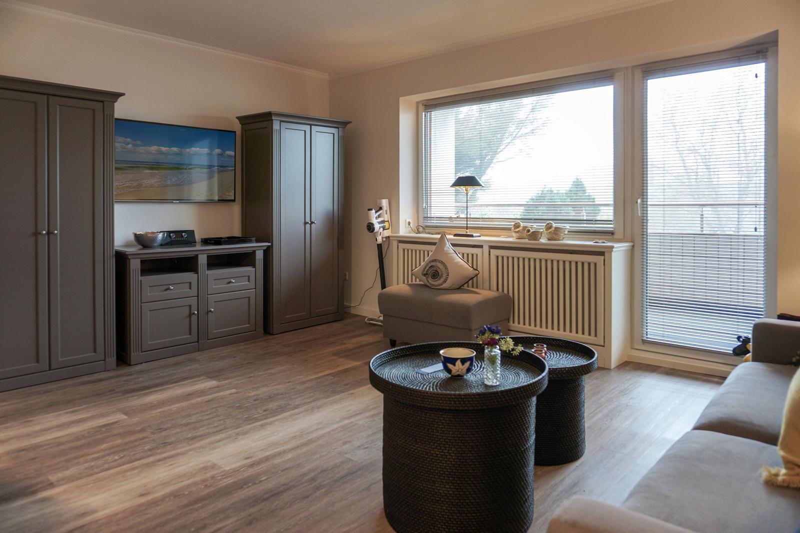 Wohnzimmer mit TV, Schränken und Fenster mit Jalousien.