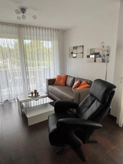 Wohnzimmer mit Sofa, Sessel und Fenster mit Jalousie.
