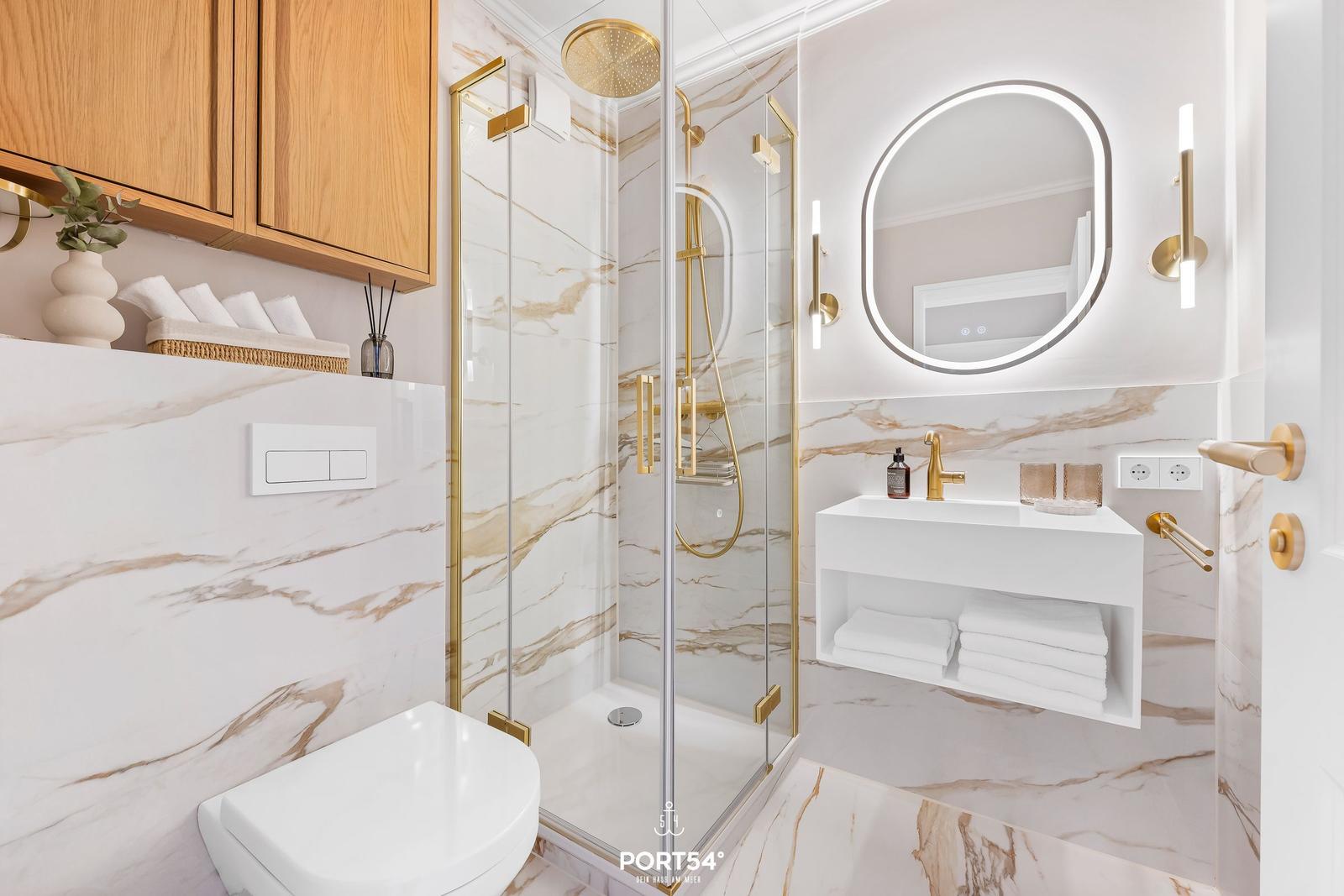 Bathroom with shower, sink, and toilet. Marble wall and gold accents.