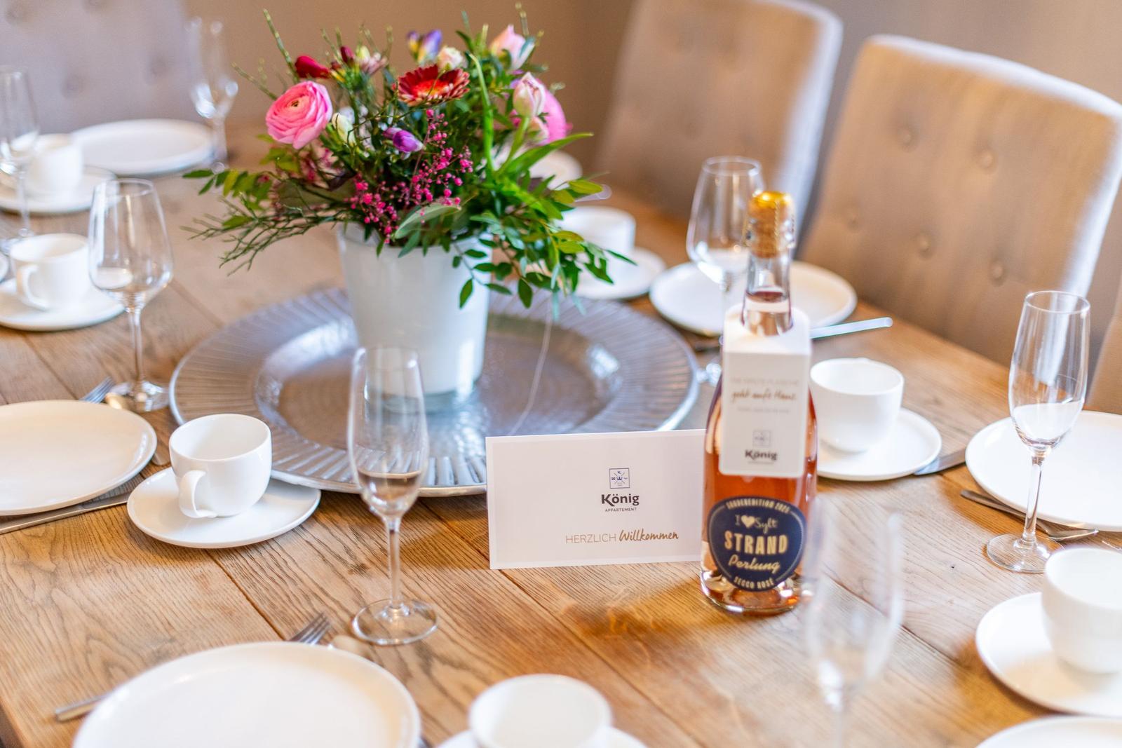 Set dining table with flower vase, glasses, and bottle.