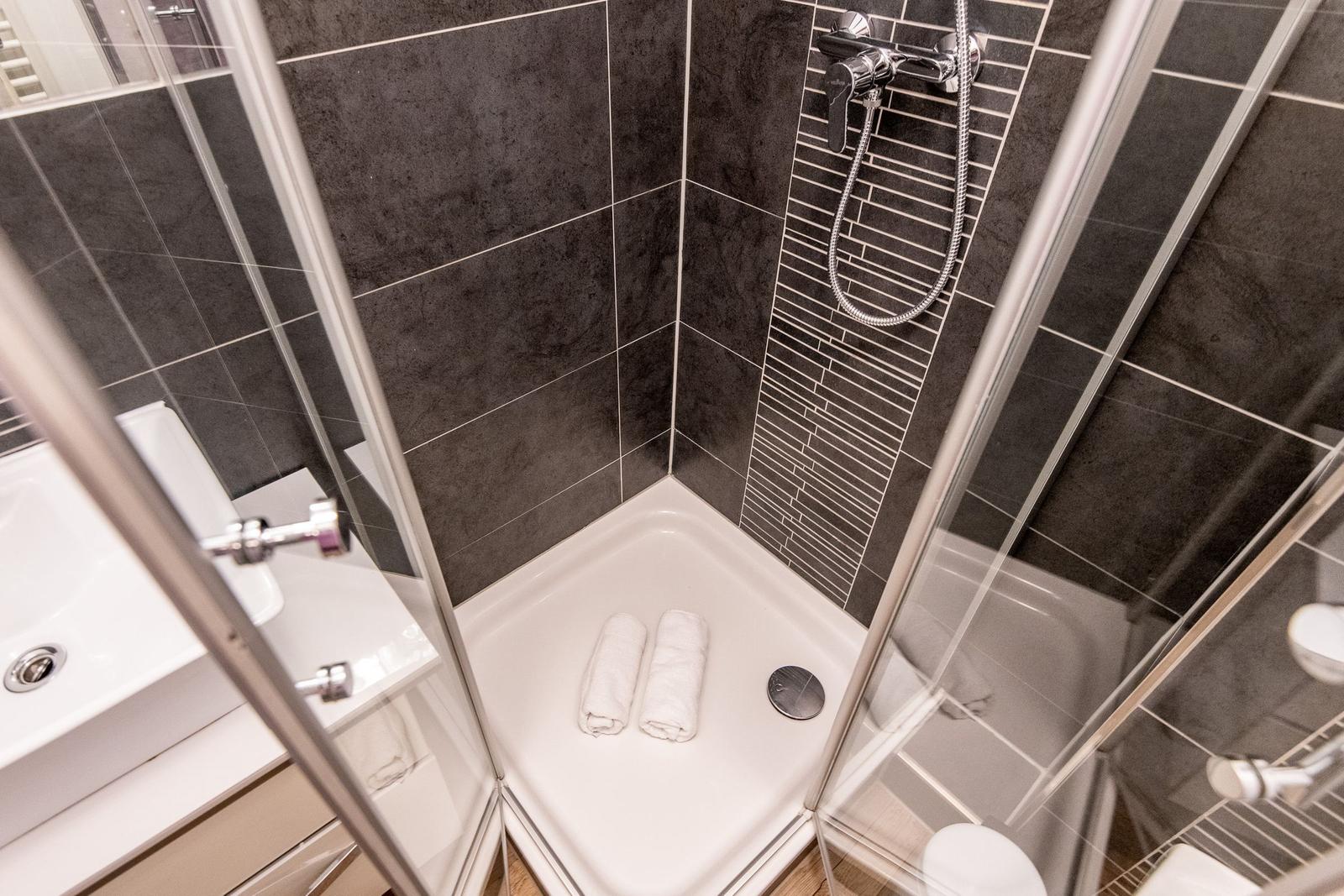 Shower cabin with dark tiles and white towels