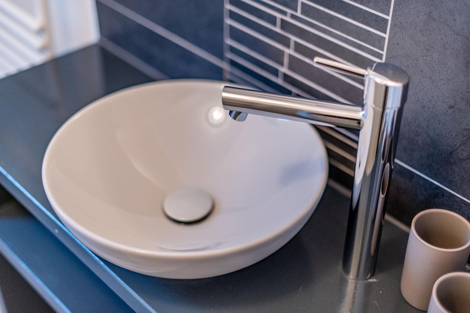 Round sink with modern faucet on dark countertop.