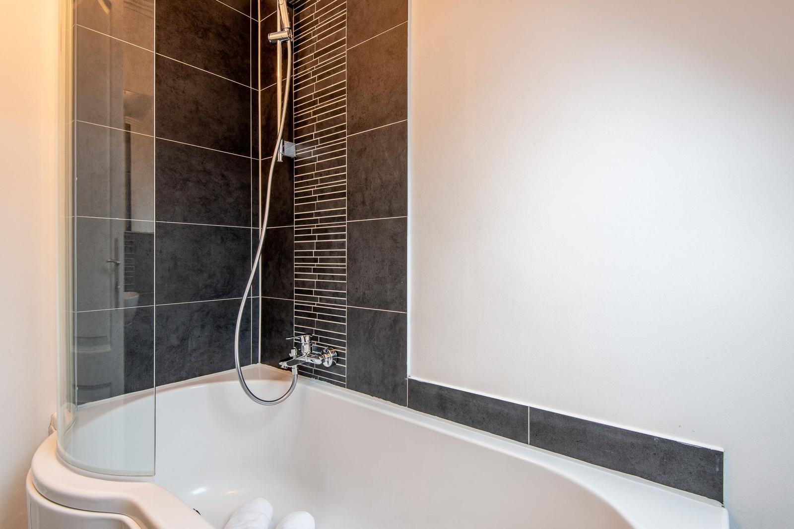 Bath with bathtub and shower with dark tiles