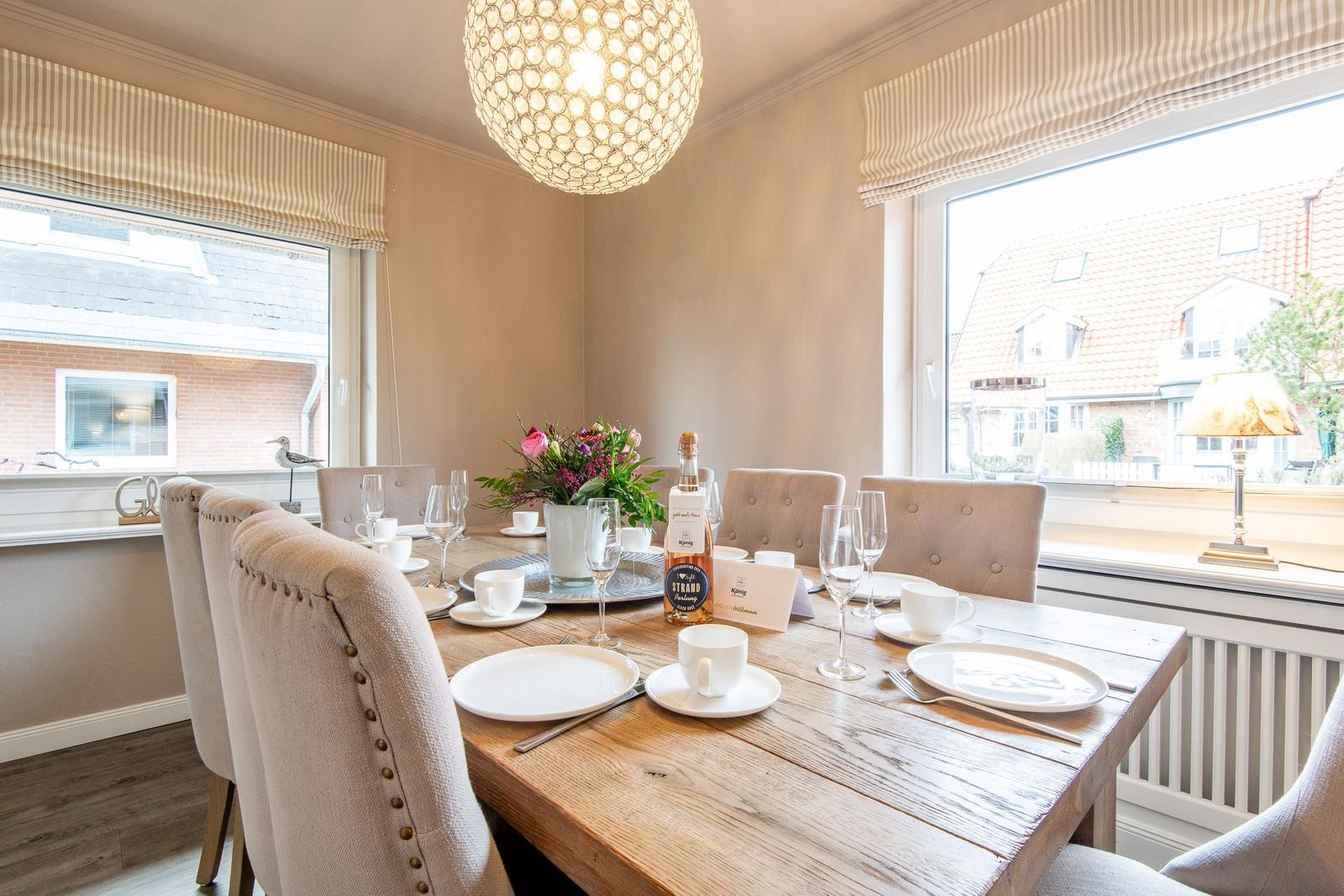Dining table with chairs, flowers, and wine bottle by windows overlooking houses.