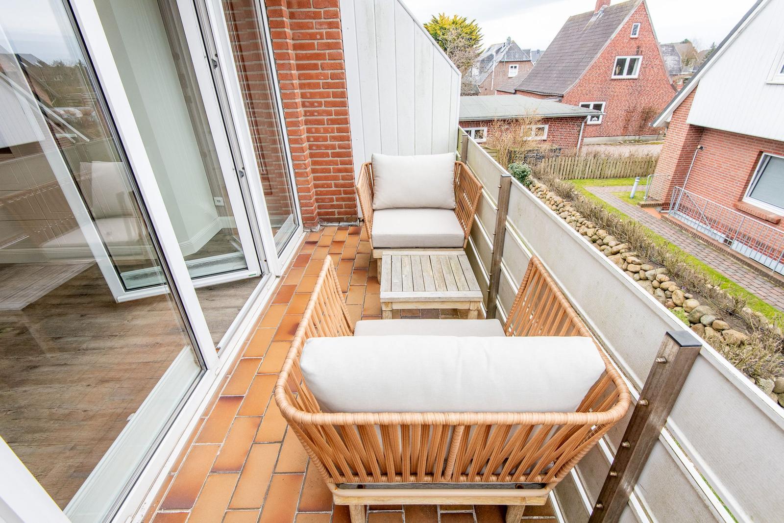 Terrace with two rattan sofas and wooden table. View of residential area with red houses.