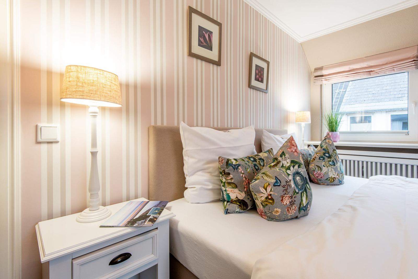 Bedroom with bed, nightstand, and window. Walls covered with striped wallpaper.