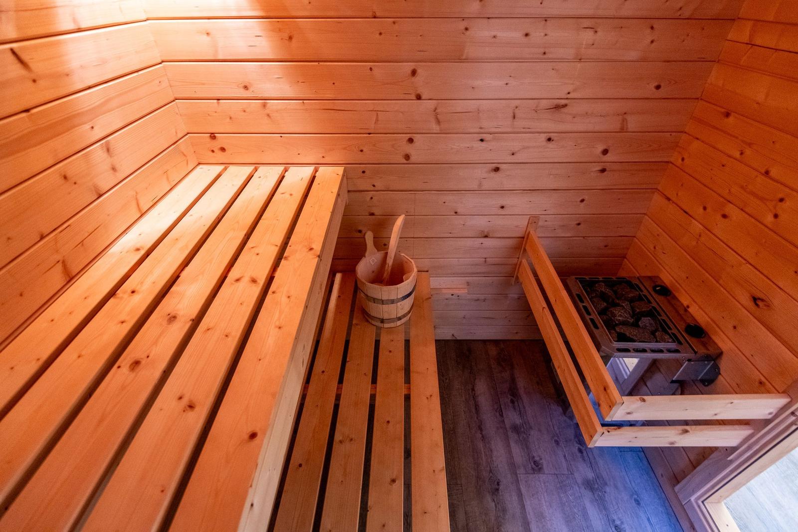 Sauna with wooden bench, bucket, and stone heater.