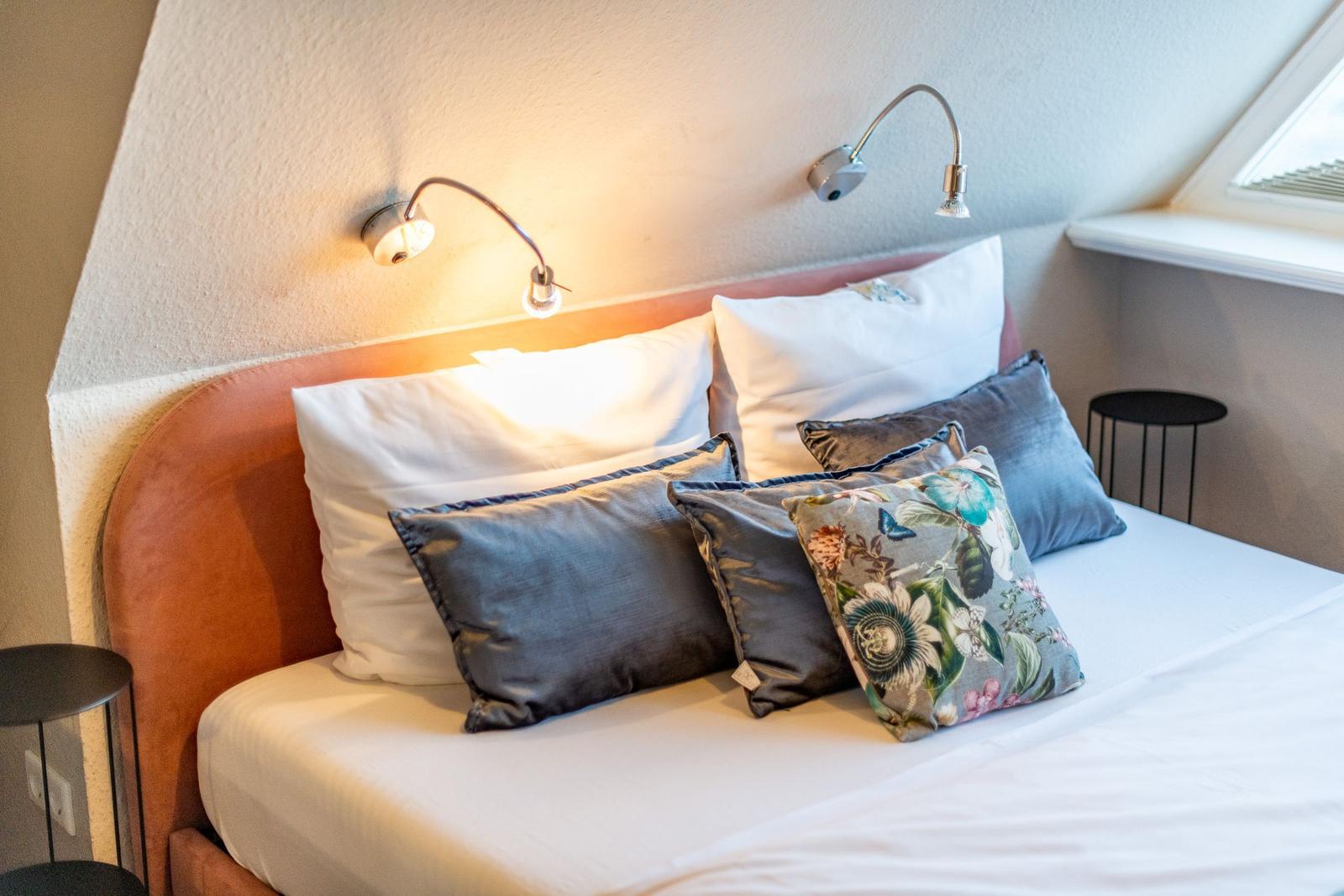 Double bed with pillows and wall lamps under sloped ceilings