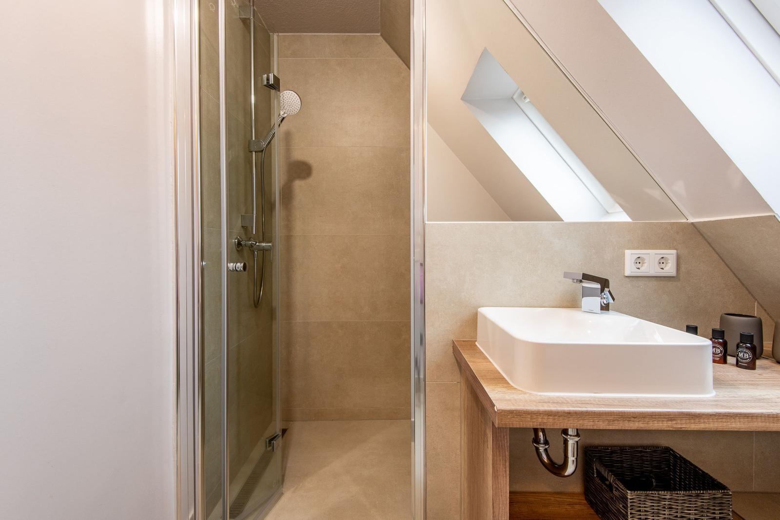 Shower with glass enclosure and sink under sloped ceiling.