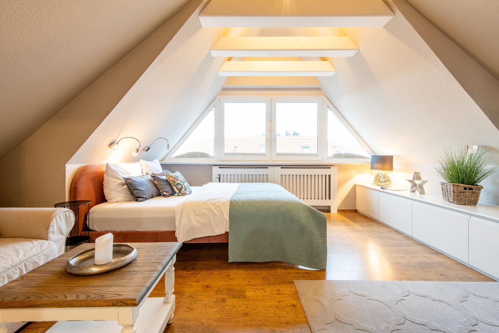 Bedroom with sloped ceilings, large window, and wooden floor.