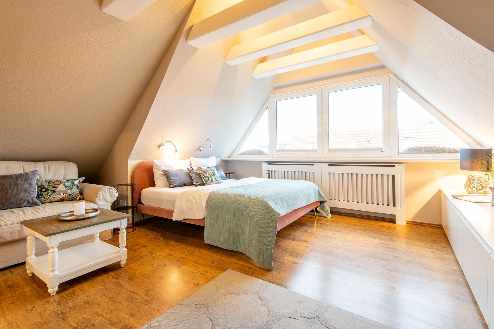 Bedroom with sloped ceiling, bed, sofa, and wooden floor.