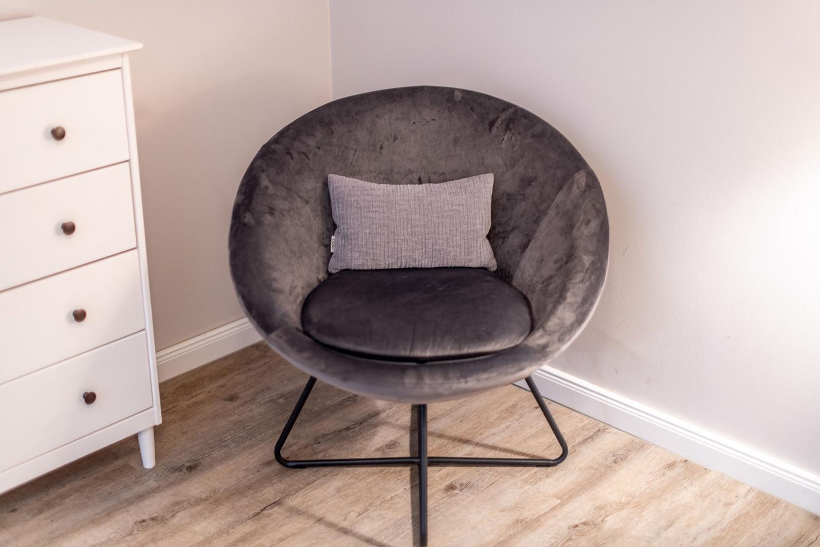 Round gray seating with pillow next to white dresser.