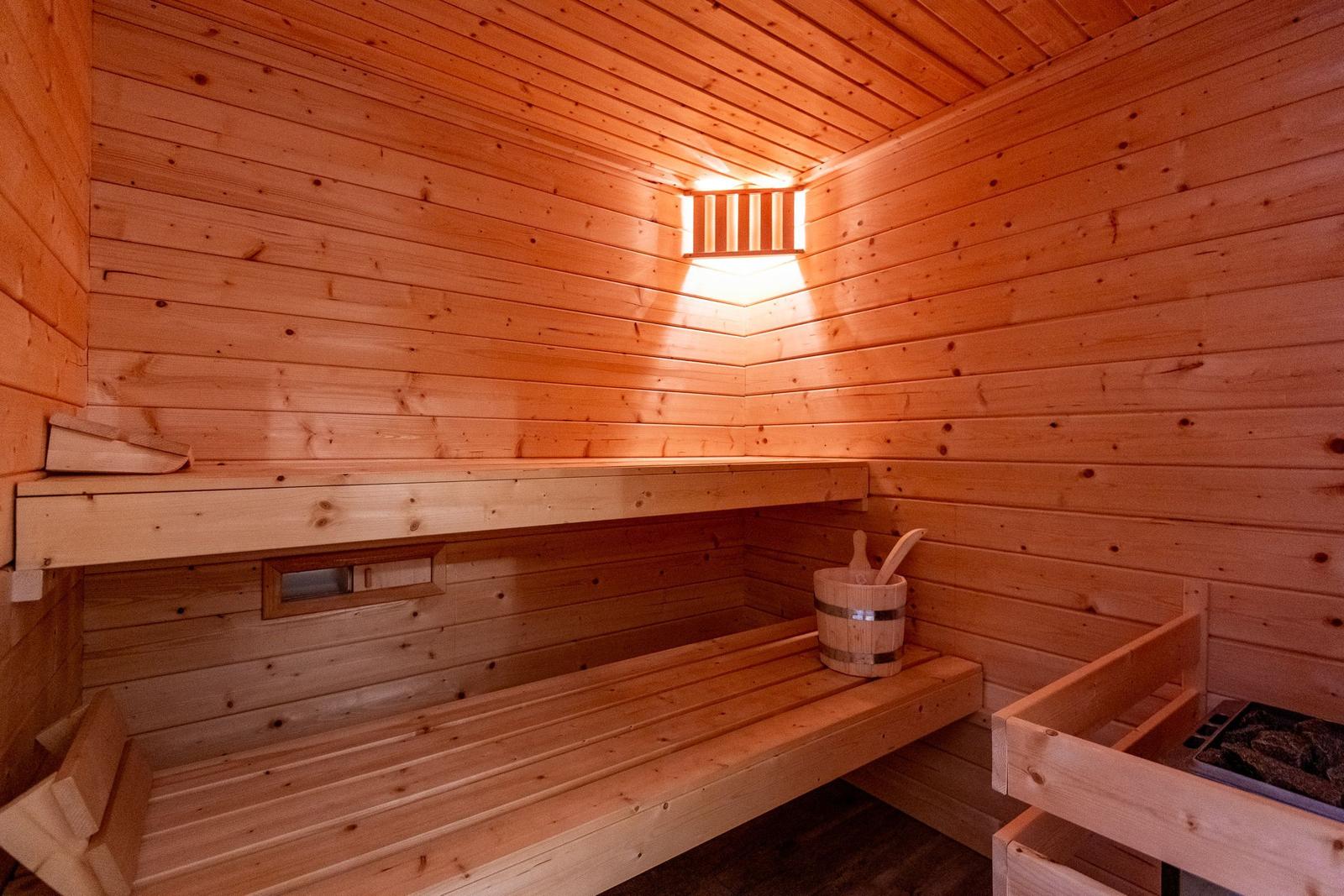Wooden sauna with bench, bucket, and steam vent.