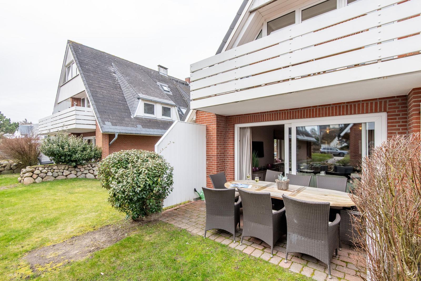 Terrace with table and chairs, garden and house with balcony.