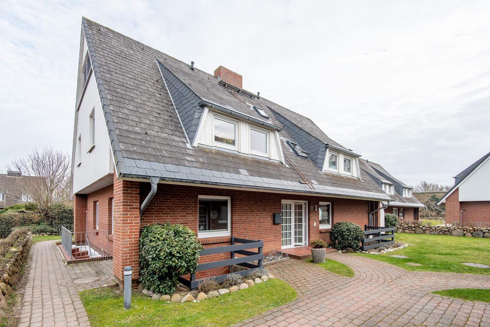 House with red brick and gray roof, lawn and paved path in front.