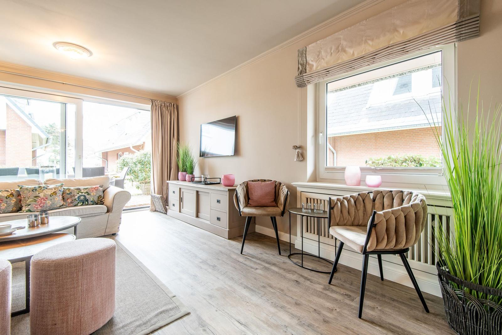 Living room with sofa, chairs, and TV. Large windows and wooden floor.