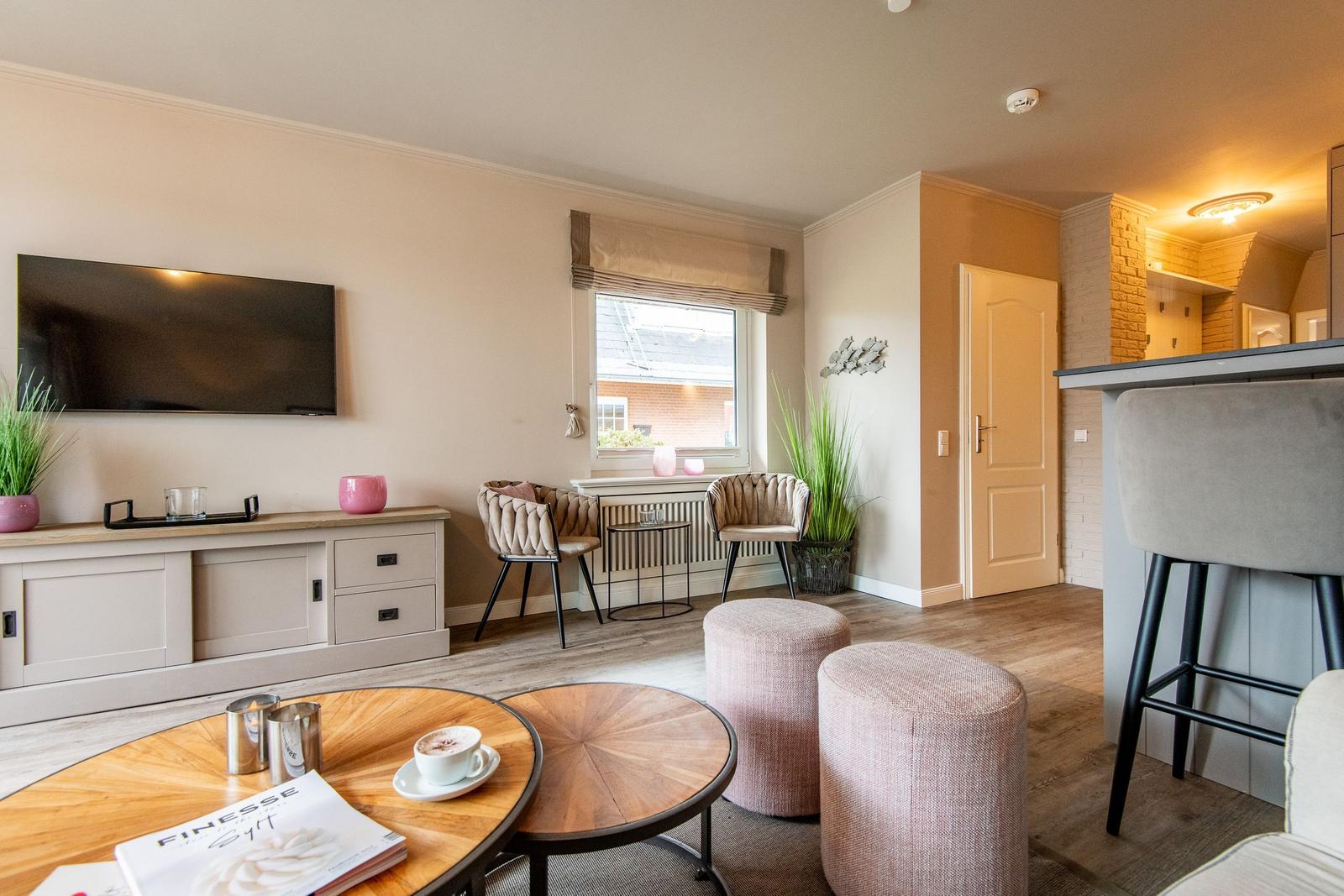 Living area with TV, seating, and window. Wooden table, plants, and bar stools visible.