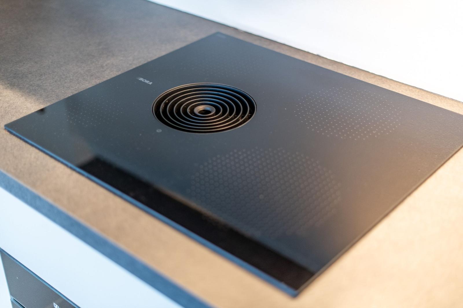 Schwarze Induktionskochplatte mit Ventilationsöffnung und Markenlogo.