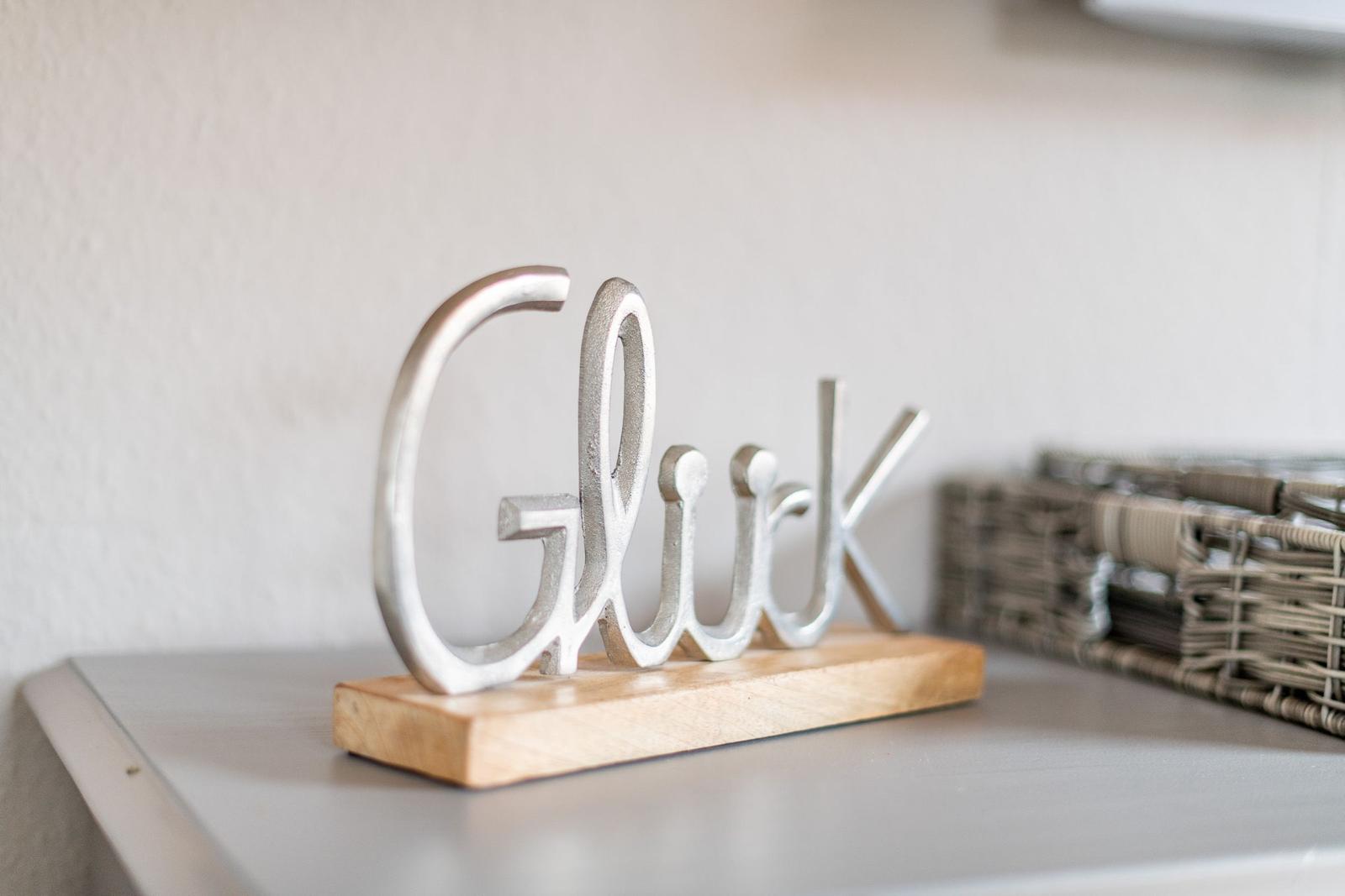 Metall-Schriftzug Gluck auf Holzsockel auf Schrank