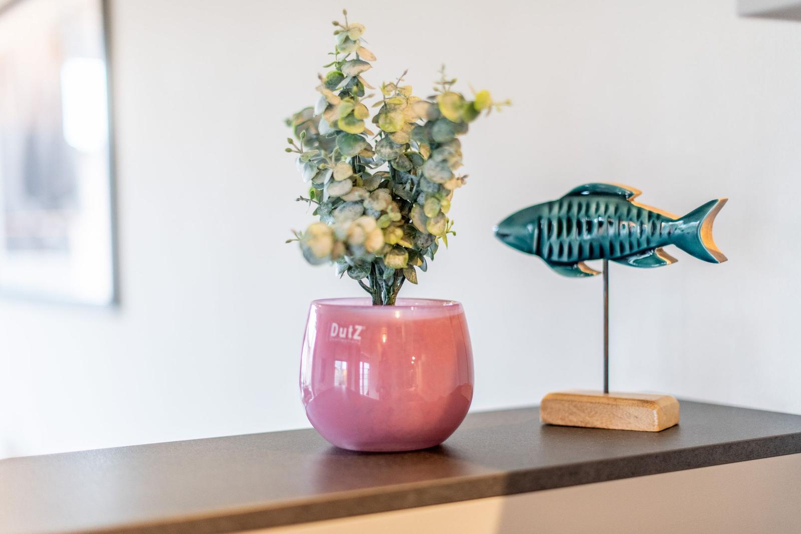 Auf der Arbeitsplatte steht eine rosa Vase mit grüner Pflanze und eine dekorative Fischfigur.