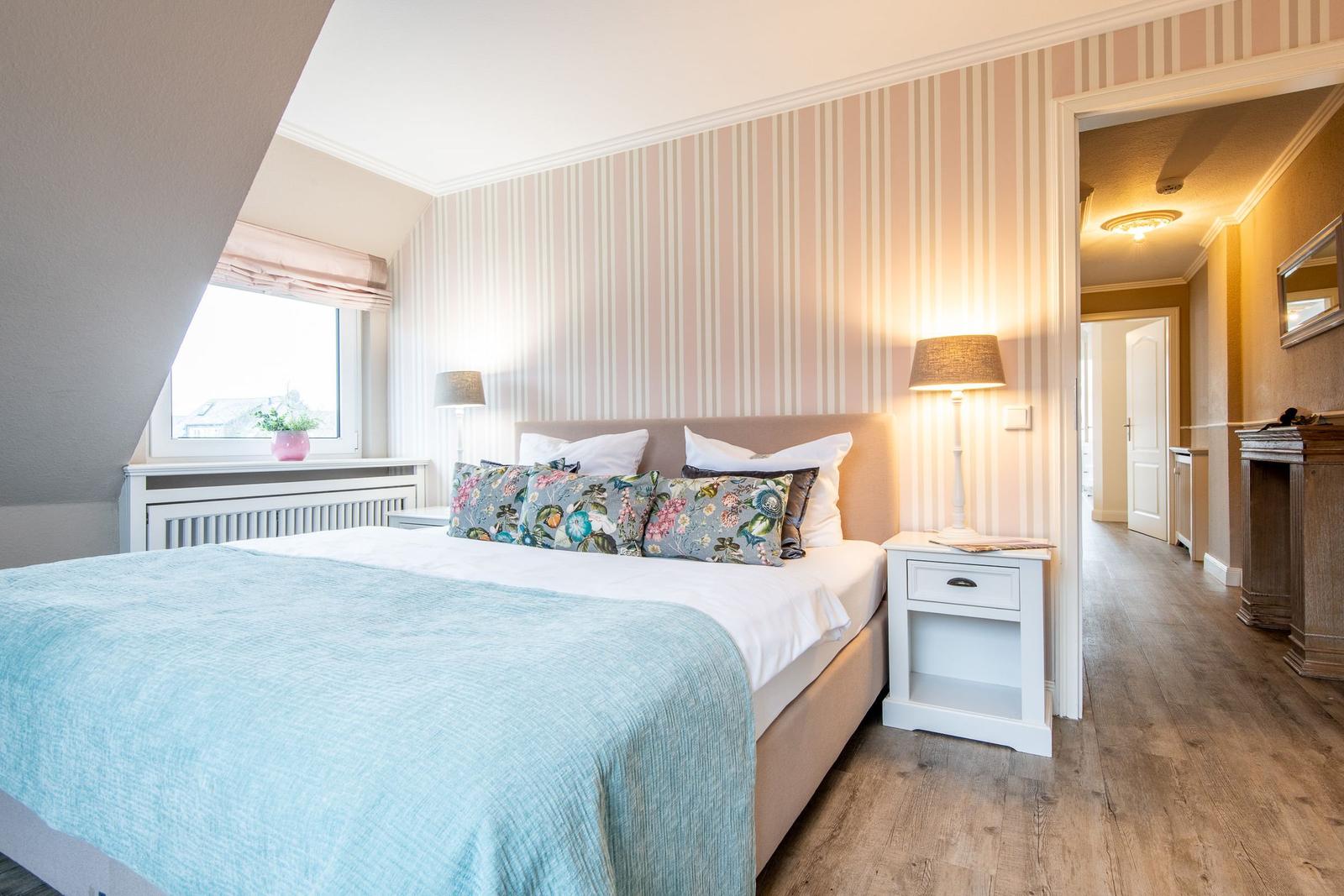 Schlafzimmer mit Bett, Nachttisch und Fenster. Wand mit Streifenmuster.