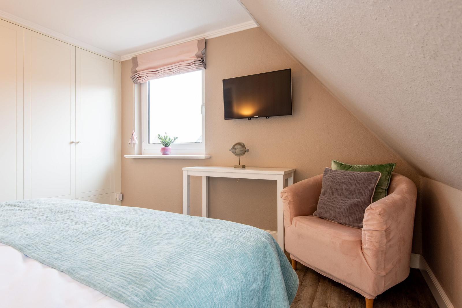 Schlafzimmer mit Bett, Kleiderschrank, Sessel und TV an der Wand.