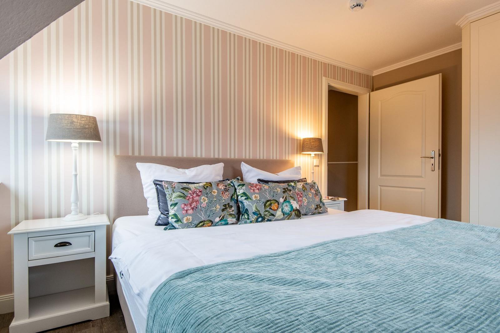 Schlafzimmer mit Bett, Nachttisch und gestreifter Wandtapete.