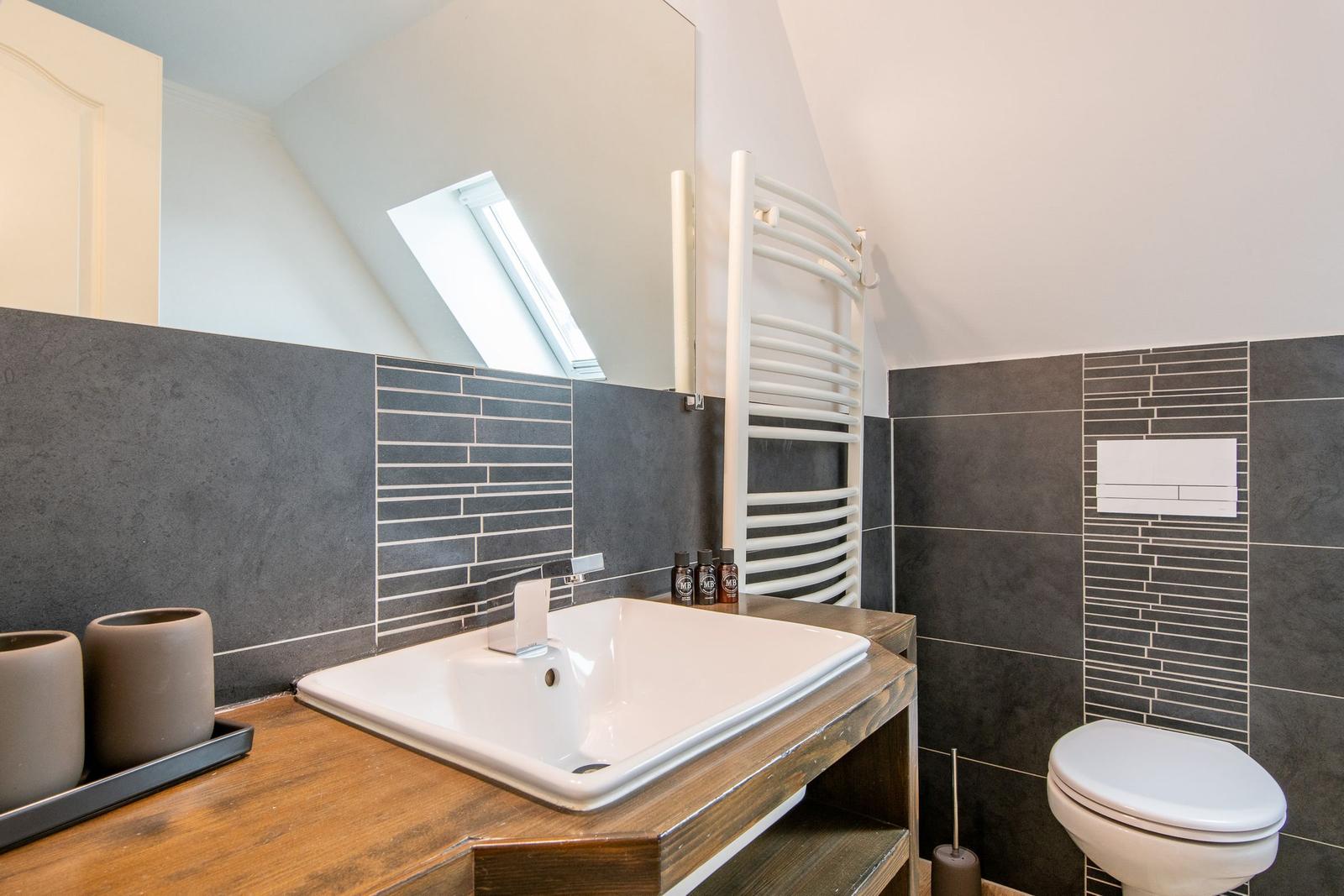 Badezimmer mit Waschbecken, Toilette und Heizkörper an schräger Decke.