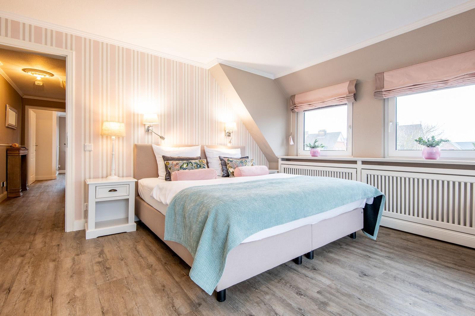 Schlafzimmer mit Bett, Nachttisch und Fenstern. Wandverkleidung und Holzboden.