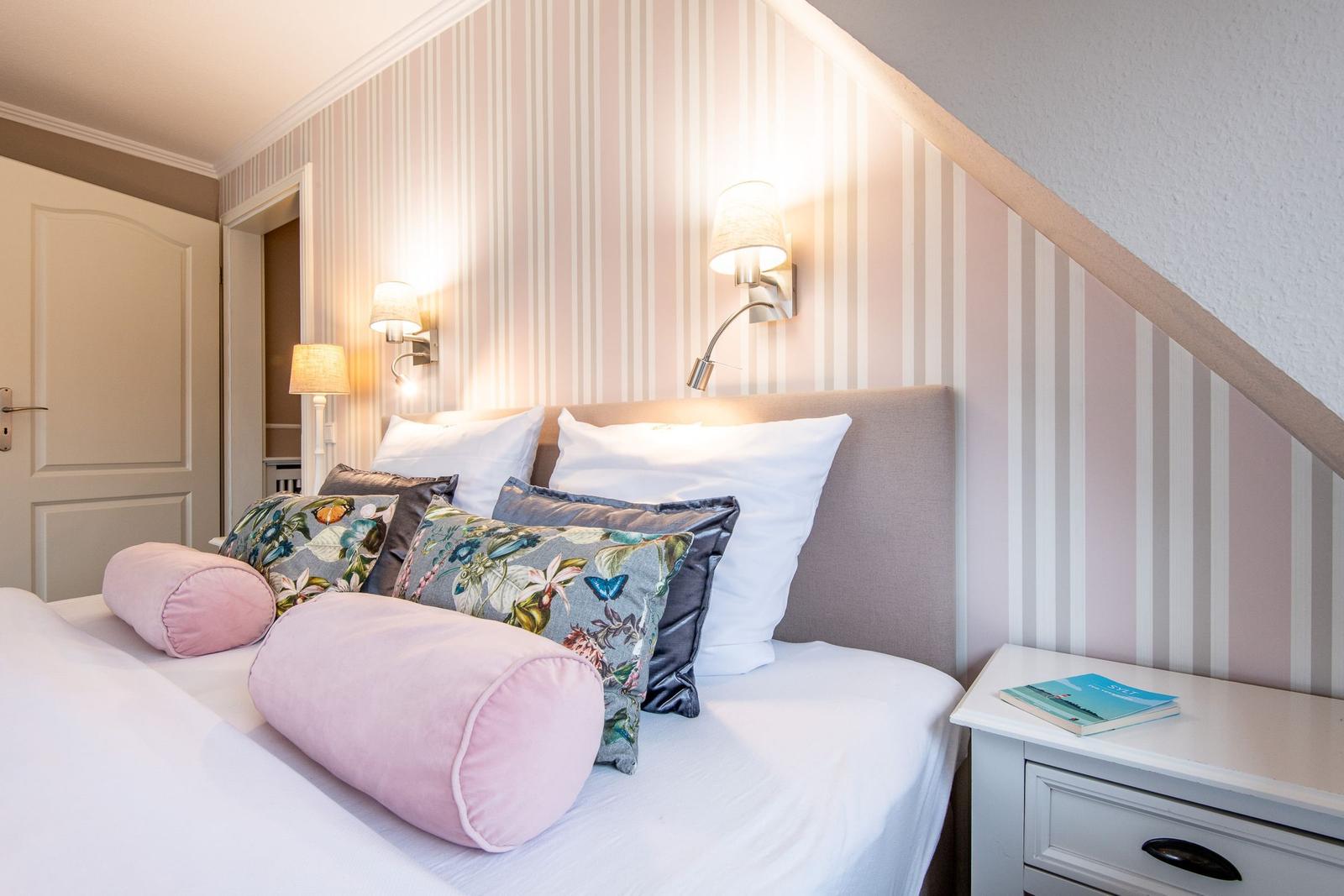 Schlafzimmer mit Bett, Kissen und Wandbeleuchtung. Streifenwand und Nachttisch.