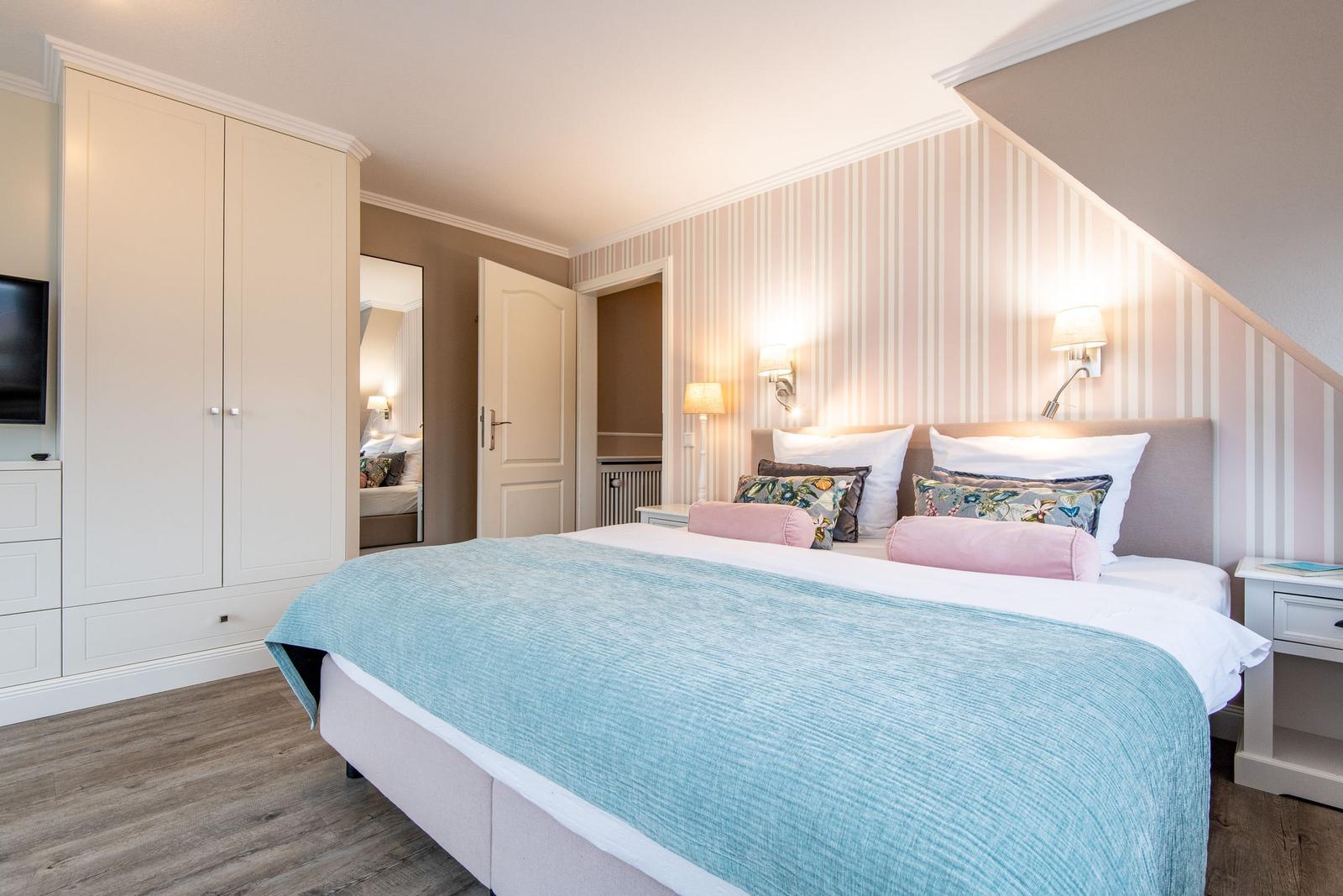 Schlafzimmer mit Bett, Kleiderschrank und Wandbeleuchtung.