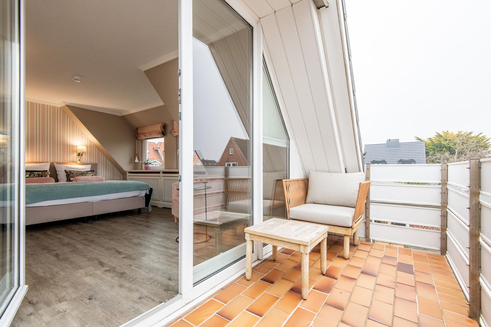 Dachgeschosszimmer mit Schlafbereich und Balkon mit Sitzgelegenheit.