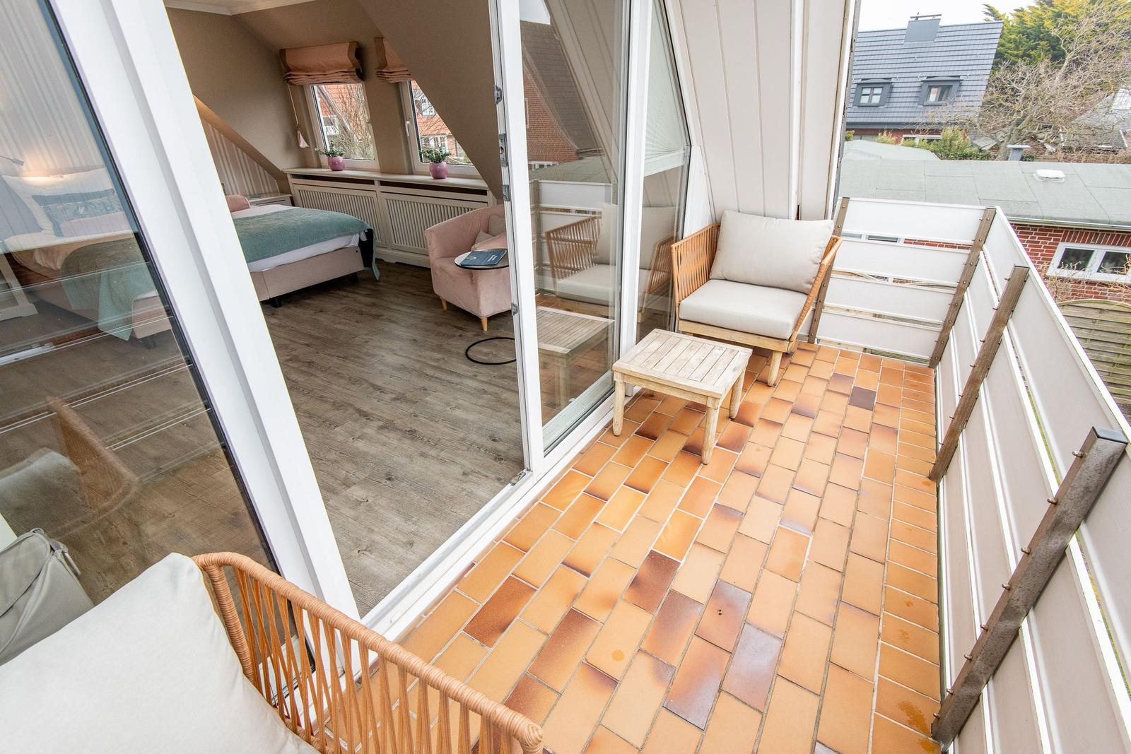 Terrasse mit Sitzgelegenheit und Blick in Schlafzimmer mit Bett und Fenstern.